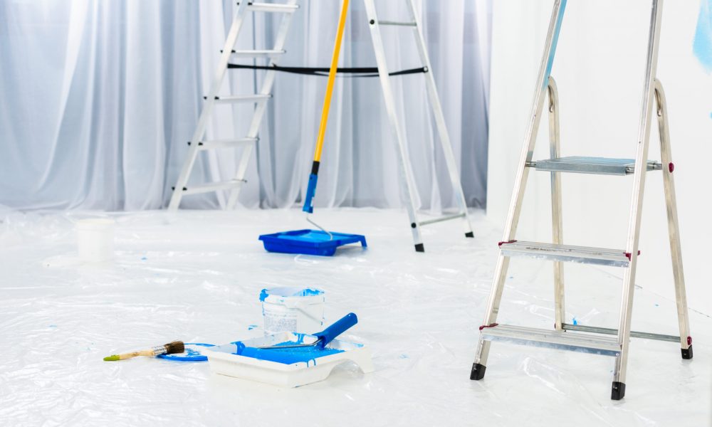 ladders and paint roller brushes in blue paint in room